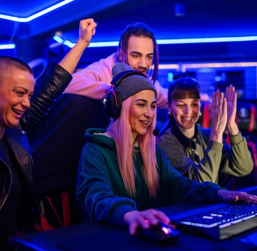 Gamer girl playing a video game in cybercafe while friends cheering.
